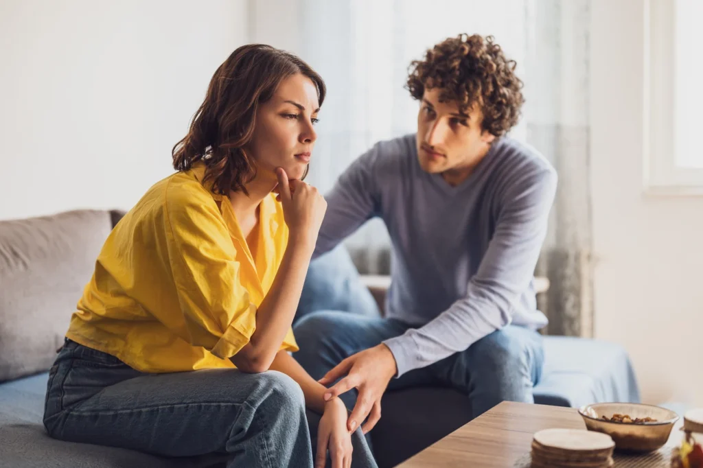 Pareja joven sentada en el sofá del salón durante una conversación tensa